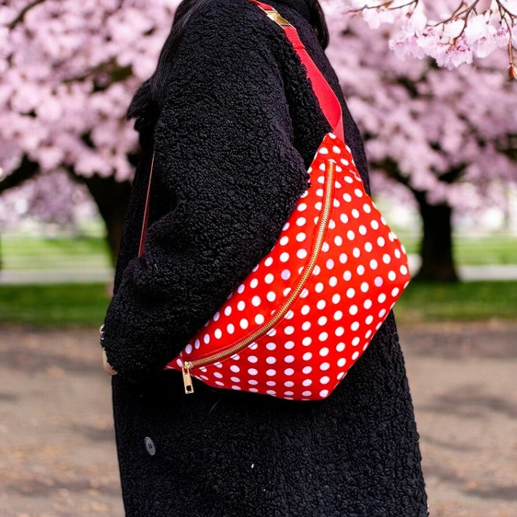 Femme portant un sac banane rouge à pois blancs en bandoulière sur manteau noir — accessoire rétro chic pour voyage et sorties